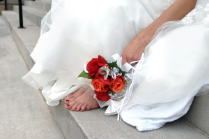 A Bride has taken off her uncomfortable shoes and is sitting down and resting her feet
